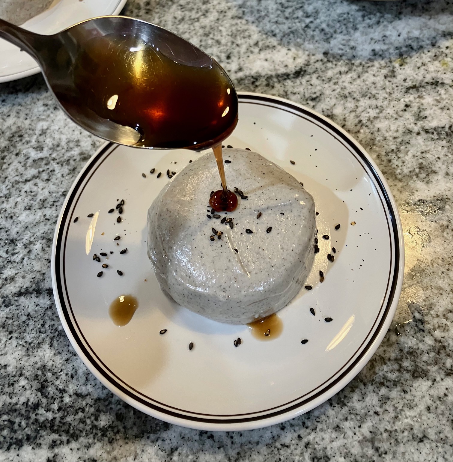 Black sesame panna cotta on a plate with brown sugar syrup being drizzled on top