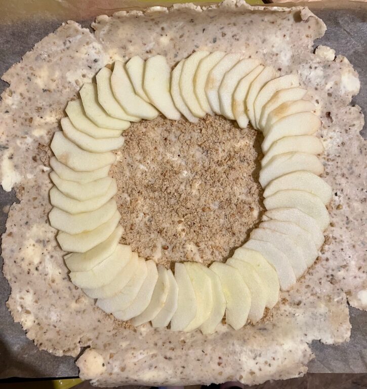 Galette dough covered with a layer of brown sugar and walnuts, and one ring of apples, with a thick border around the edge