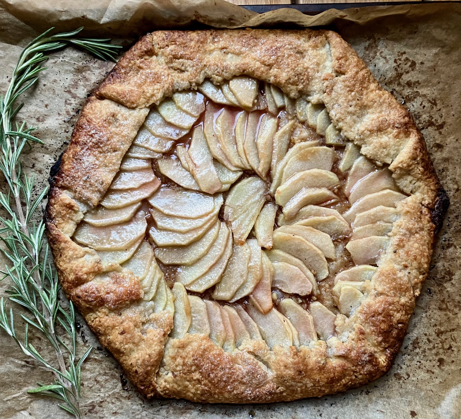 Apple galette with rosemary and walnuts on parchment paper with sprig of rosemary