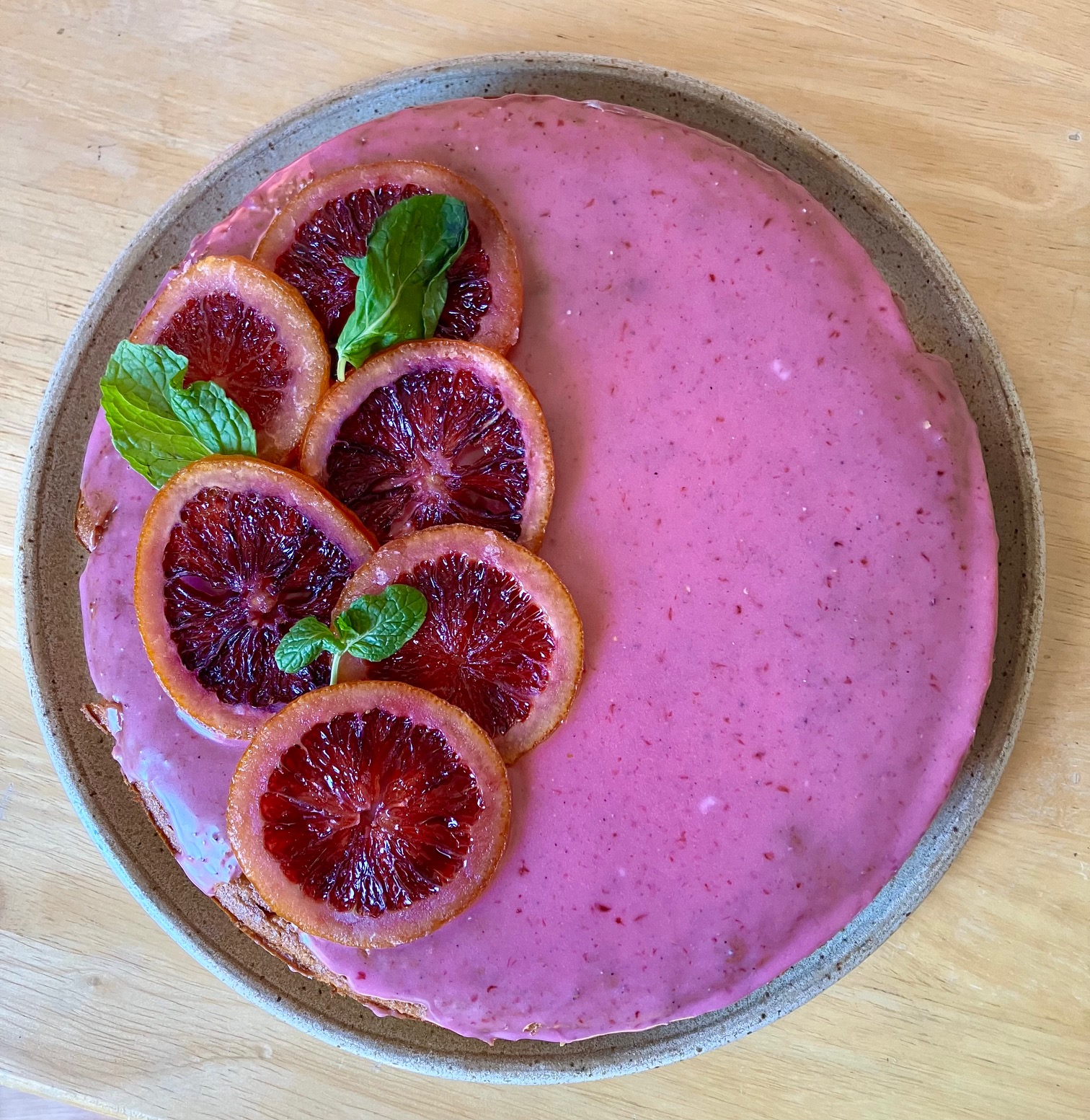 Blood orange cake with cardamom on a plate with candied blood oranges arranged on the left and mint leaves on top